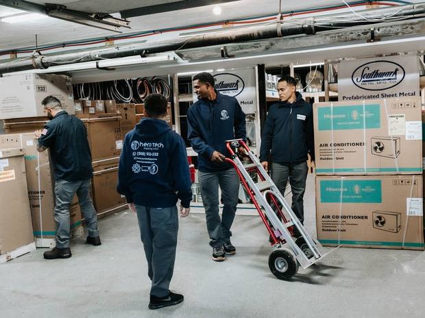Hero Tech technicians moving new air conditioning units in the company warehouse