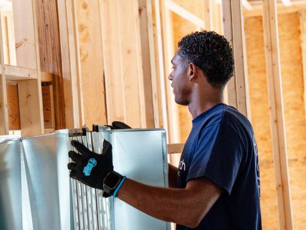 A Hero Tech technician carrying sheet metal duct sections through a framed house