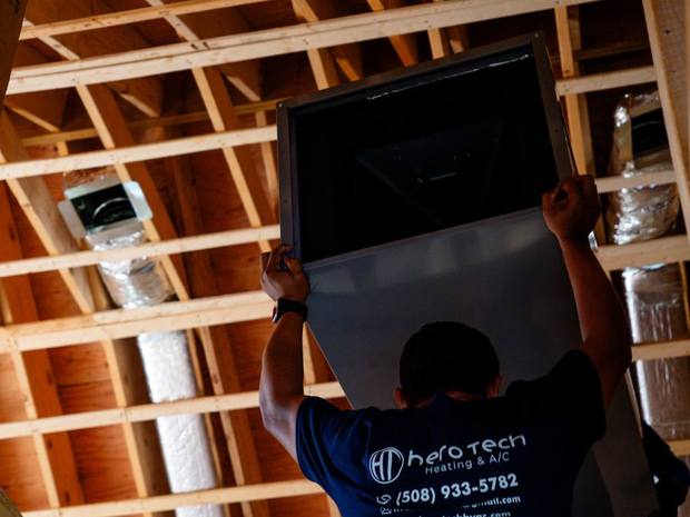 A Hero Tech technician lifting a new air handler into a ceiling during a heating installation