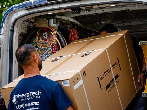 A Hero Tech technician loading a ductless mini-split indoor unit into the service van